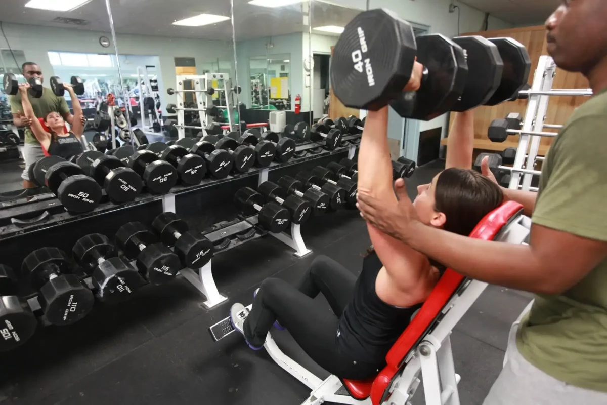 Young woman working out with dumbbells and a personal trainer in the gym