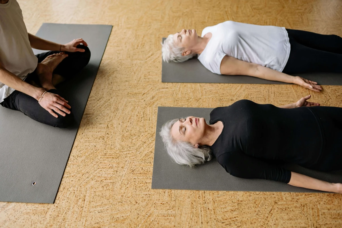 Two mature ladies on a mat on the floor of a studio meditating