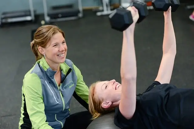 Two smiling women exercising with gym in the background