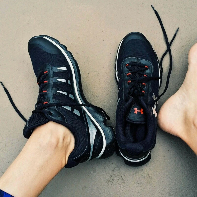 A pair of black with white stripes and orange train with the Under Armour logo